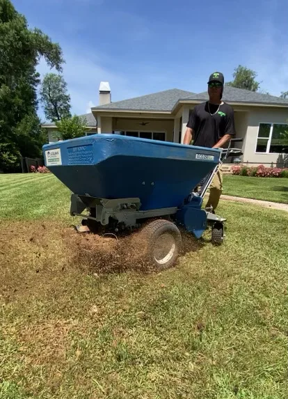 A person operating a lawn care spreader on a grassy area in Panama City, FL, highlighting the importance of professional lawn care services.